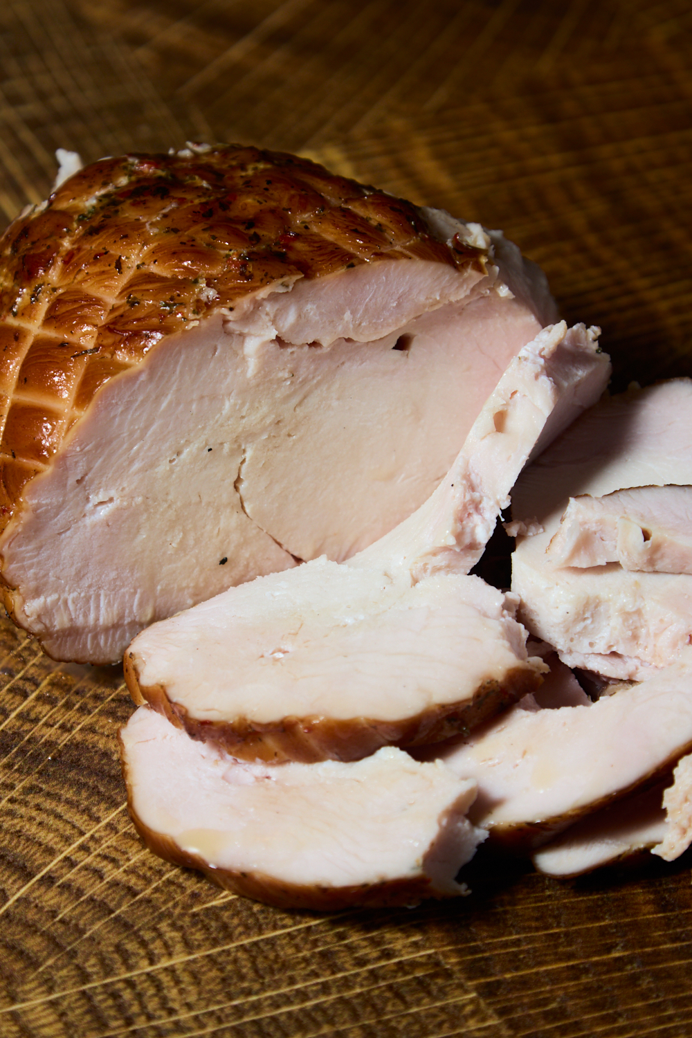 A close-up of a cooked, seasoned smoke turkey breast on a wooden surface, with several slices cut and laid in front of the main piece—prepared on a pellet smoker with no brine for simple, savory flavor.