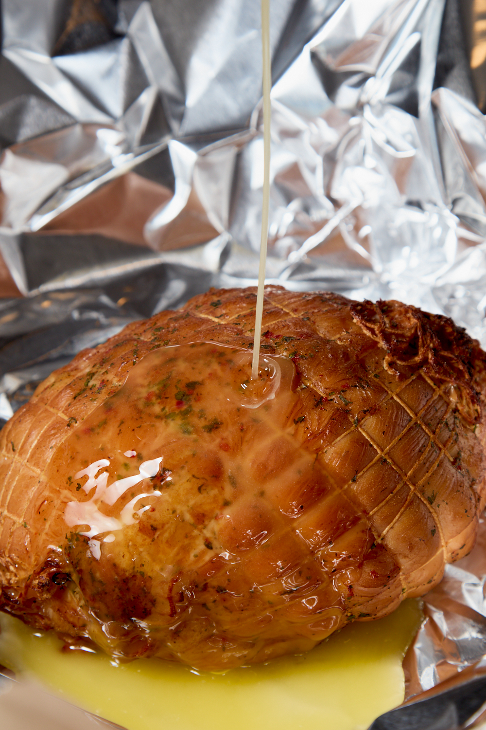 A cooked, netted roast sits on crumpled aluminum foil as melted butter or oil is poured over it, creating a shiny glaze—perfect for a no brine smoke turkey breast made on your pellet smoker.