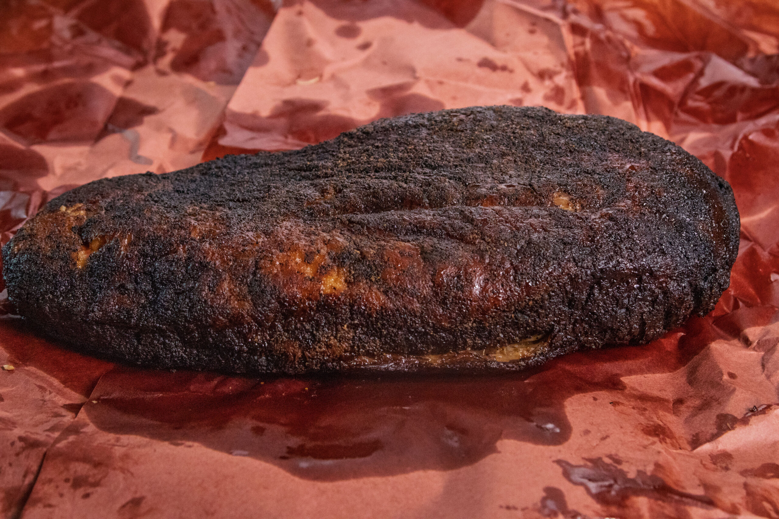 A large, darkly crusted smoked brisket rests on brown butcher paper, showing a well-cooked bark and visible meat juices—a testament to proper smoking techniques and how to trim a brisket for mouthwatering results.