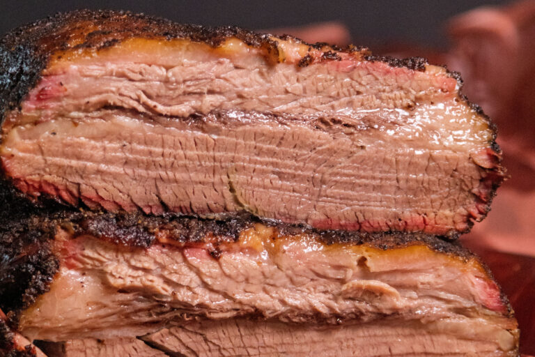 Sliced smoked brisket with dark bark and a pink smoke ring on butcher paper