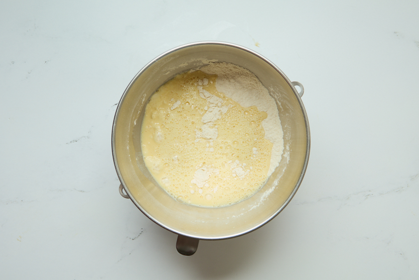 A metal mixing bowl containing partially mixed batter, with visible flour and wet ingredients on a white surface—perfect for making chewy beignets that capture the essence of classic New Orleans beignets.