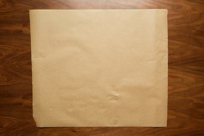A large square sheet of plain brown parchment paper lies flat on a wooden surface.